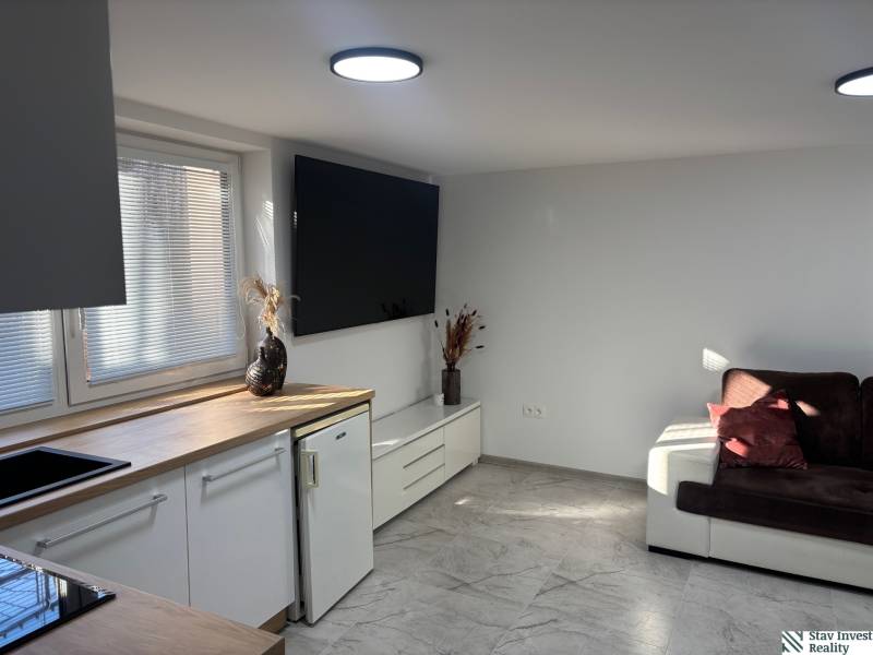 Nappali egy családi házban fehér konyhabútorral és sötétbarna kanapéval.