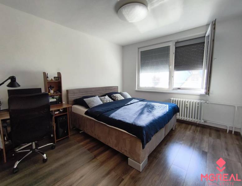 Hálószoba fa mintás padlóval, íróasztallal és ággyal egy egyszobás lakásban.