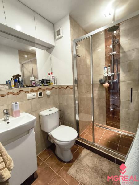 Fürdőszoba egy egyszobás lakásban, zuhanyzó, mosdó, WC és szekrények.