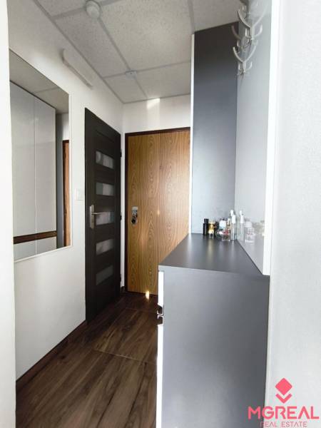 Folyosó fa mintázatú padlóval és fehér bútorokkal egy egyszobás lakásban.