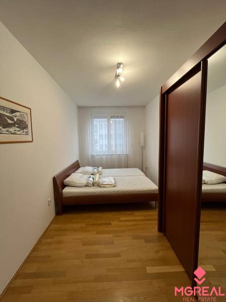 Hálószoba ággyal, beépített szekrénnyel és fa dekorációjú padlóval egy háromszobás lakásban.