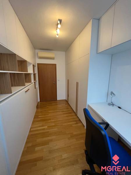 Dolgozószoba fehér bútorokkal, beépített szekrényekkel és fa dekor padlóval egy háromszobás lakásban.