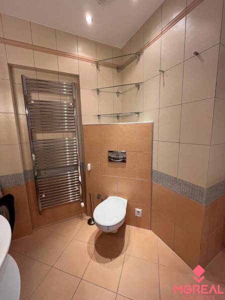 Fürdőszoba egy háromszobás lakásban csempével, WC-vel, létrás radiátorral és üvegpolcokkal.