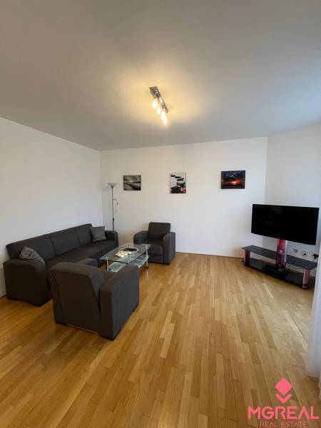 Nappali egy háromszobás lakásban, fa dekoros padlóval, kanapéval és televízióval.