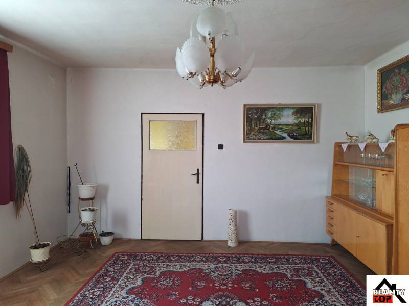 Nappali egy családi házban szőnyeggel, csillárral, képpel és vitrinnel.