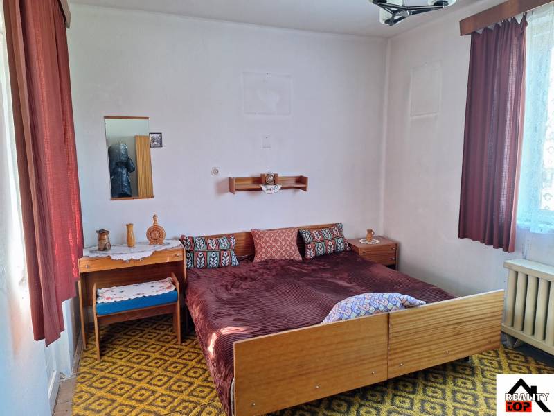 Hálószoba családi házban textilfüggönyökkel, mintás szőnyeggel és ággyal.