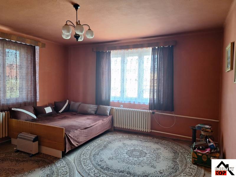 Egy szoba családi házban ággyal, szőnyeggel, függönyökkel és éjjeliszekrénnyel.