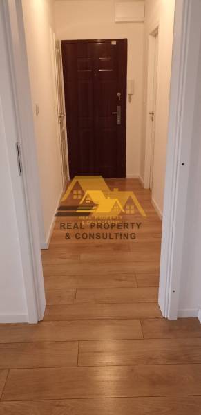 Keskeny folyosó bejárati ajtóval és fa dekorációjú padlóval egy kétszobás lakásban.