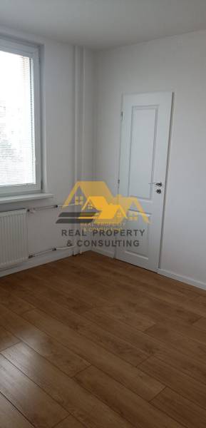 Kilátás egy két szobás lakás fehér falú és fa dekorációjú padlójú szobájára.