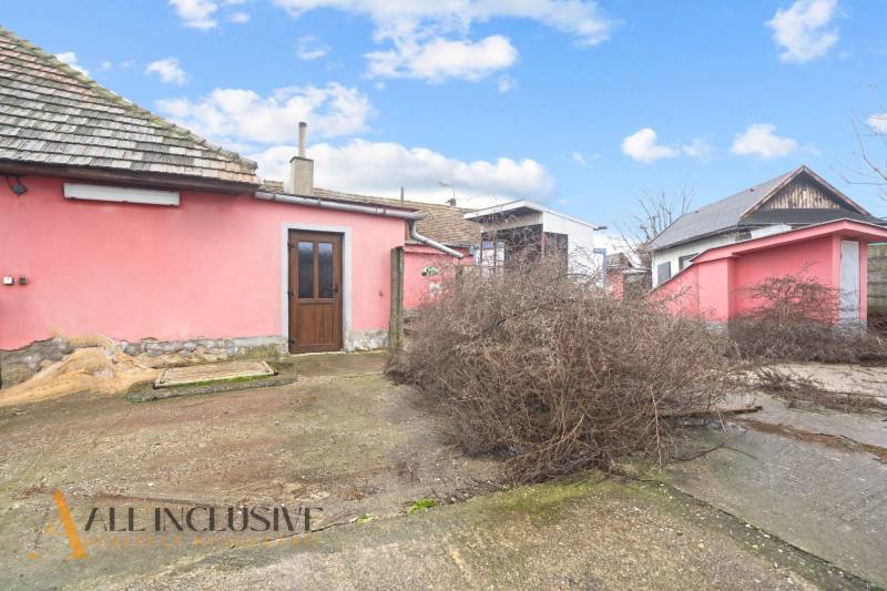 Családi ház Sempteben rózsaszín homlokzattal, gondozatlan udvarral és faajtókkal.