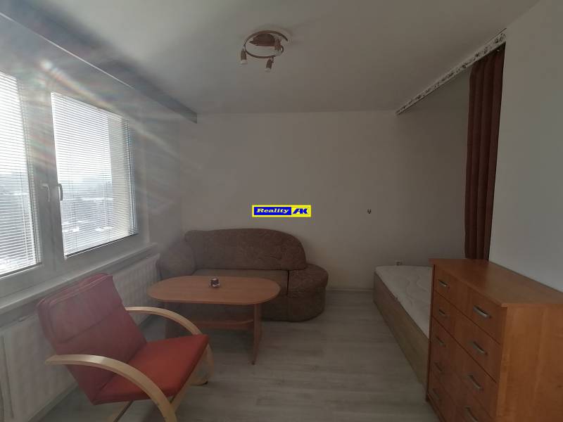 Egyszobás lakás egy székkel, asztallal és komóddal, fa dekoros padlóval.