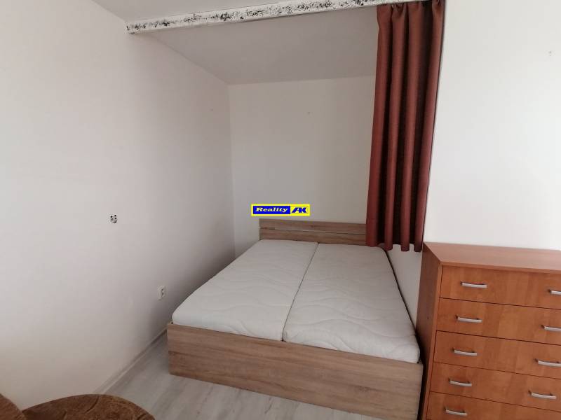 Hálószoba egy egyszobás lakásban ággyal, komóddal és fa dekorációjú padlóval.