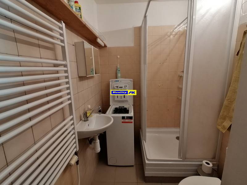 Fürdőszoba egy egyszobás lakásban mosdóval, zuhanyzóval és mosógéppel.