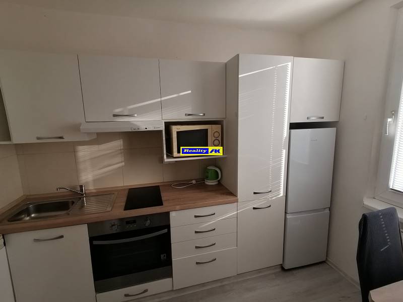 Konyha egy egyszobás lakásban, gépekkel és fehér bútorokkal.