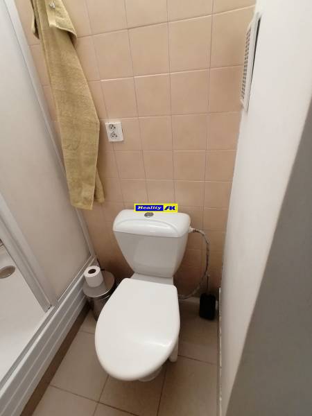 Fürdőszoba egy egyszobás lakásban WC-vel, zuhanyzóval és bézs csempékkel.