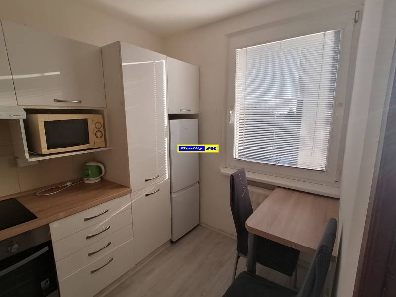 Konyha egy egyszobás lakásban, készülékekkel és redőnyös ablakkal.