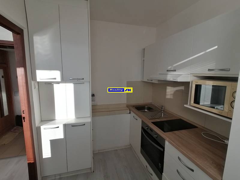 Konyha egy egyszobás lakásban, fehér szekrények, mosogató, főzőlap, mikrohullámú sütő, fa dekor padló.