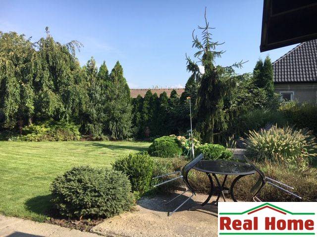 Családi ház kertje Feketevízen gyeppel, fákkal és kerti ülőgarnitúrával.