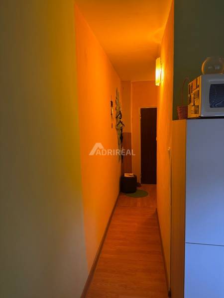 Keskeny folyosó egy egyszobás lakásban, fa dekorációjú padlóval és finom világítással.