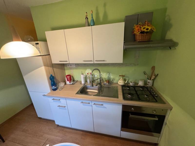 Konyha egy egyszobás lakásban fehér szekrényekkel és fa dekorációjú padlóval.