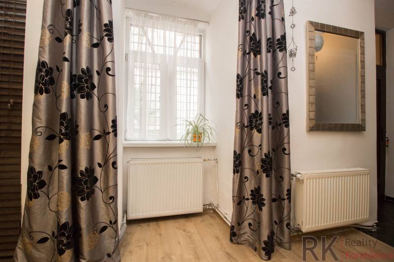 Szoba egy kétszobás lakásban, fa dekoros padlóval, függönyökkel és egy virággal a párkányon.