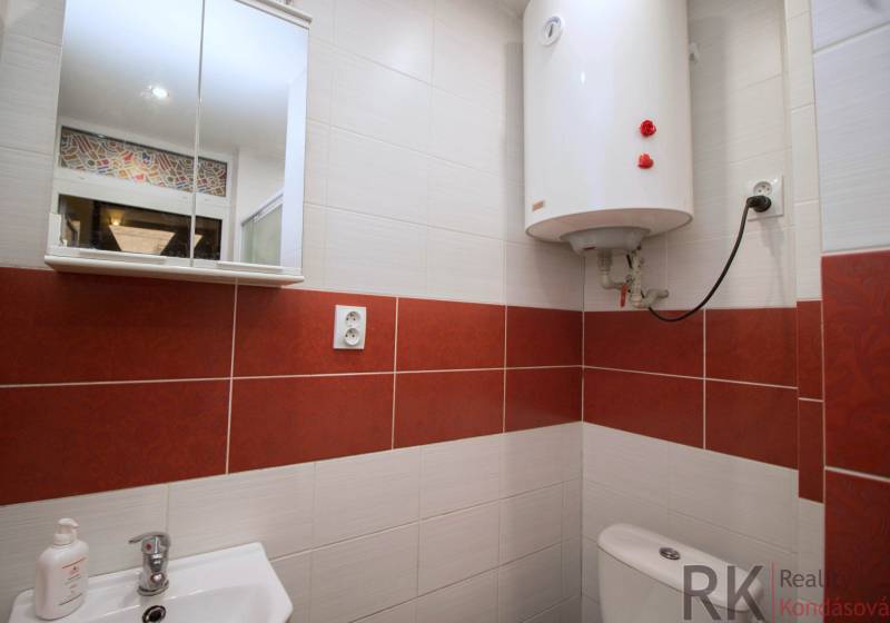 Fürdőszoba fehér bojlerrel, mosdóval és tükrös szekrénnyel egy kétszobás lakásban.