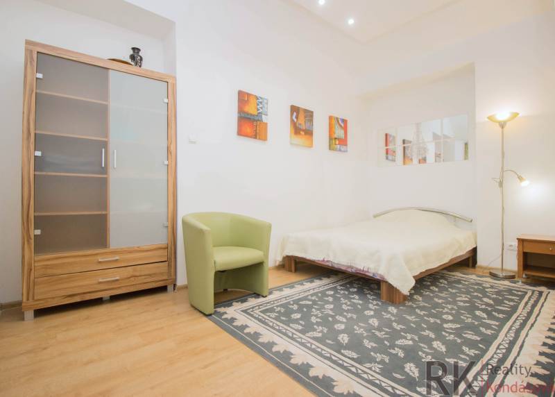 Hálószoba egy kétszobás lakásban, fa dekorációjú padlóval, szőnyeggel és ággyal.