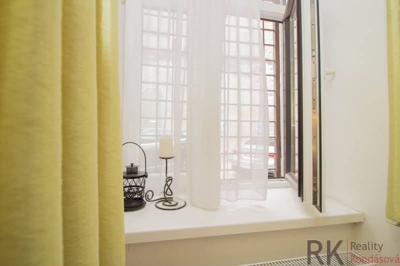 Nyitott ablak egy kétszobás lakásban, függönyökkel és dekorációkkal a párkányon.