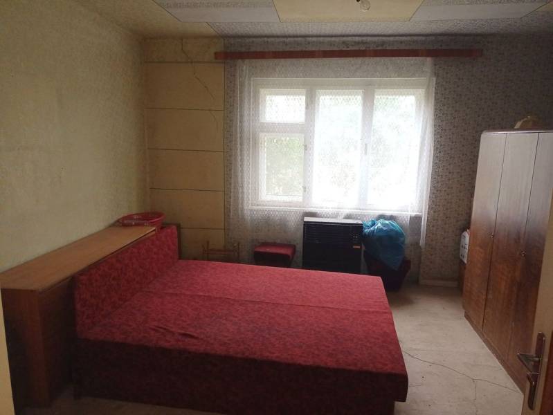 Hálószoba egy családi házban egyszerű bútorokkal és piros ággyal.