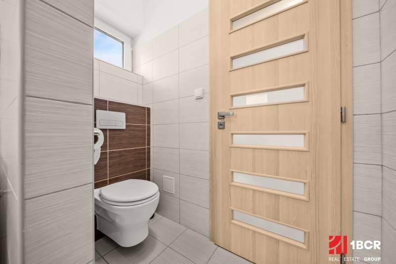 WC egy családi házban világos csempékkel és függőleges csíkos ajtókkal.