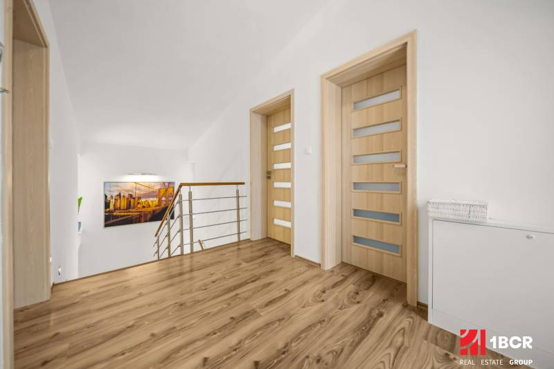 Folyosó egy családi házban fa mintázatú padlóval, minimalista korláttal és művészi fényképpel.