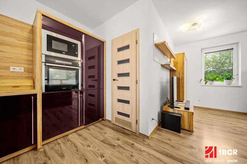 Családi ház konyhája fa hatású padlóval, modern készülékekkel és lebegő polcokkal.