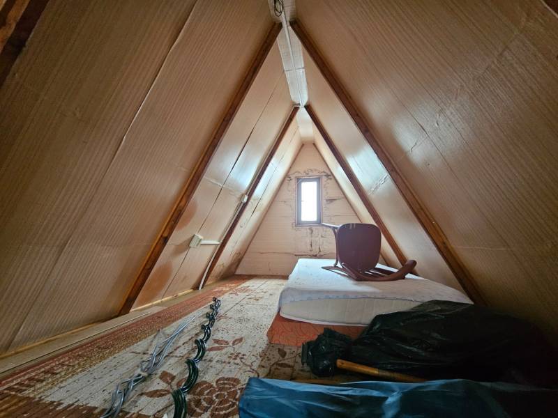 A kunyhó padlása matraccal és székkel, fa dekoráció, világos falak.