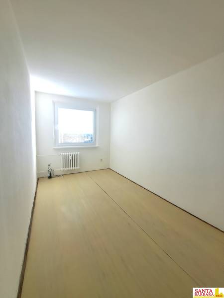 Szoba egy négy szobás lakásban fehér falakkal és fa dekorációjú padlóval.