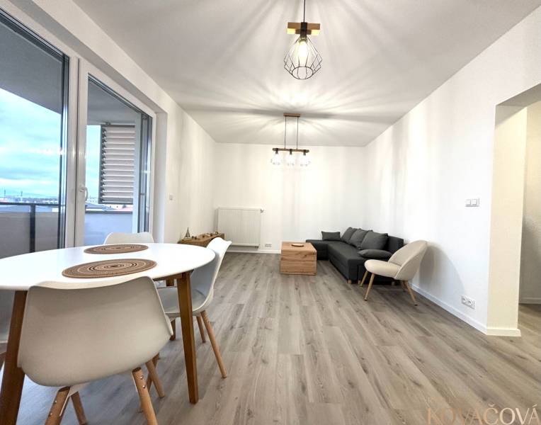 Nappali egy háromszobás lakásban kanapéval, asztallal és fa dekorációjú padlóval.