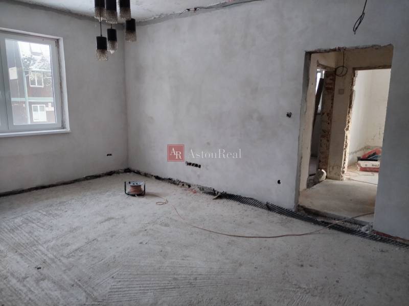 Családi ház belső tere építés alatt, csupasz falakkal és betonpadlóval.