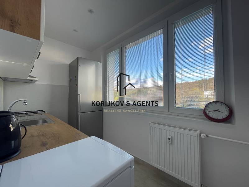 Konyha egy háromszobás lakásban, kilátással a redőnyökön keresztül, egyszerű berendezéssel és készülékekkel.