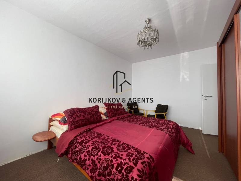 Hálószoba mintás ágyneművel, mennyezeti lámpával és gardróbszekrénnyel egy háromszobás lakásban.