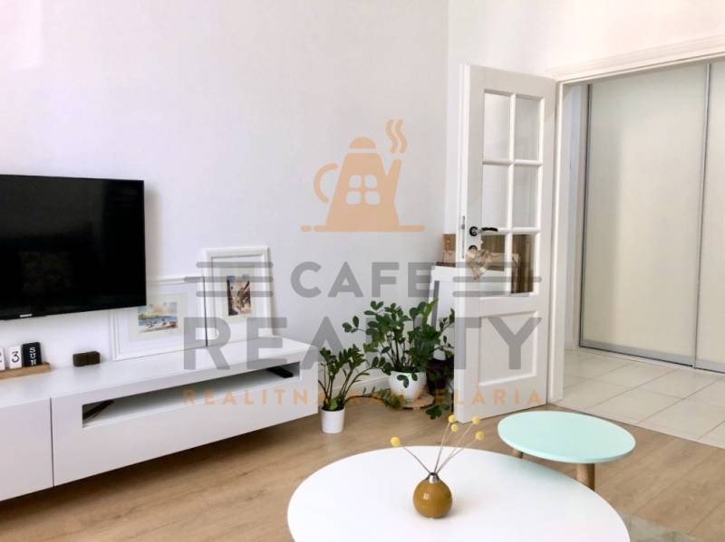 Nappali egy kétszobás lakásban, TV-vel, asztallal és fa dekor padlóval.