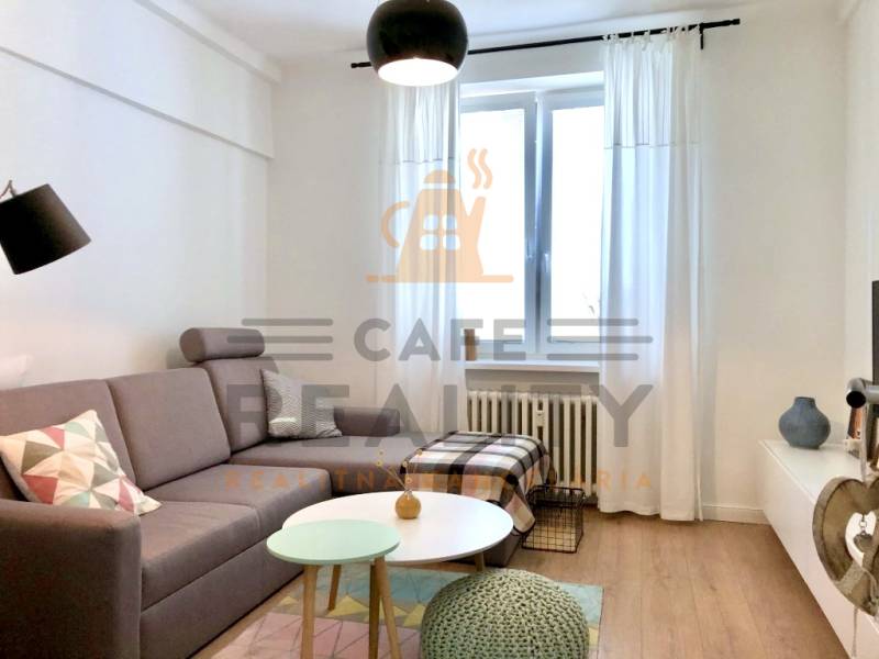 Nappali egy kétszobás lakásban szürke kanapéval és fa dekorációjú padlóval.