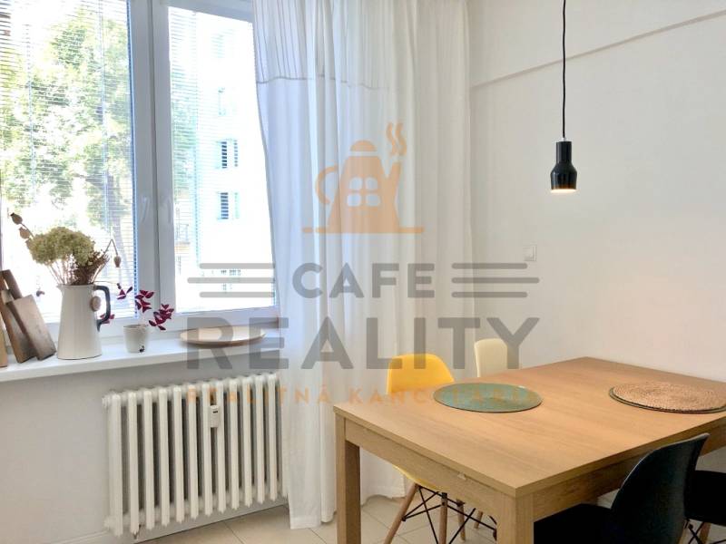 Lámpa a faasztal fölött, fehér függönyök és virágdekoráció az ablakpárkányon egy kétszobás lakásban.