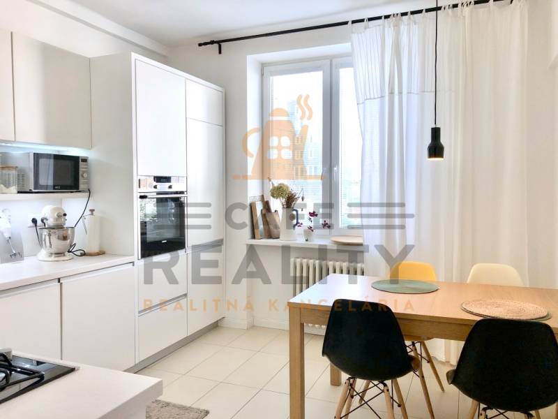 Konyha egy kétszobás lakásban fehér szekrényekkel és étkezőasztallal székekkel.