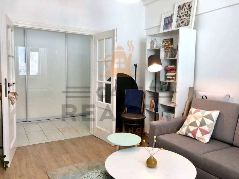 Nappali fa hatású padlóval, kanapéval és könyvespolccal egy kétszobás lakásban.