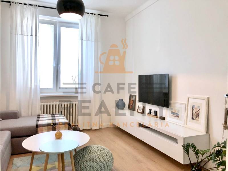 Nappali egy kétszobás lakásban, televízióval, kanapéval és fa dekorációjú padlóval.