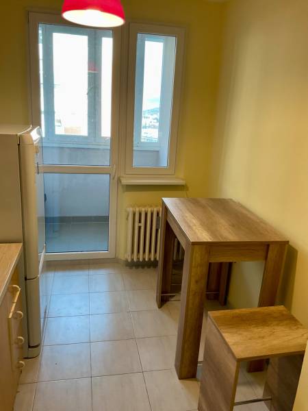 Konyha egy háromszobás lakásban nagy ablakokkal, bárasztallal és székekkel.