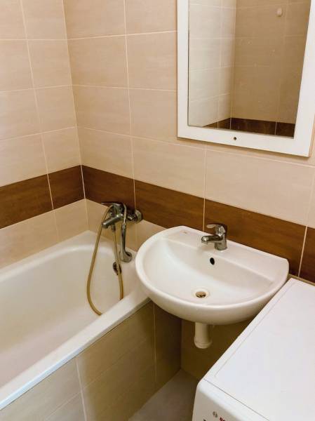 Fürdőszoba káddal, mosdóval és mosógéppel egy háromszobás lakásban, világos csempékkel.