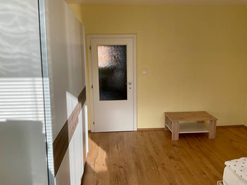 Szoba fa dekor padlóval, világos falakkal és egyszerű bútorokkal egy 3 szobás lakásban.