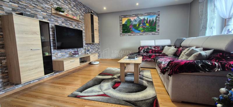 Nappali egy családi házban, fa dekoros padlóval, kővel a falon és kényelmes kanapéval.