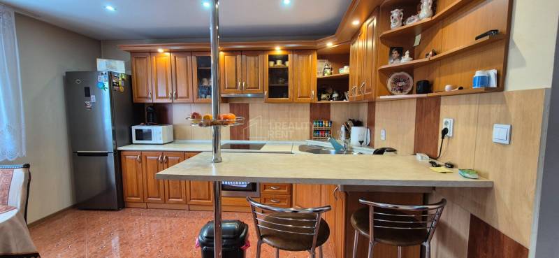 Konyha egy családi házban fa szekrényekkel, bárpulttal és háztartási gépekkel.