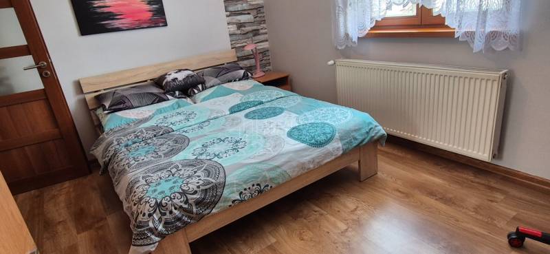 Hálószoba családi házban ággyal, radiátorral és fa dekorációjú padlóval.